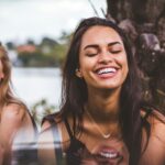 Two women happily laughing together outdoors by a serene lakeside.